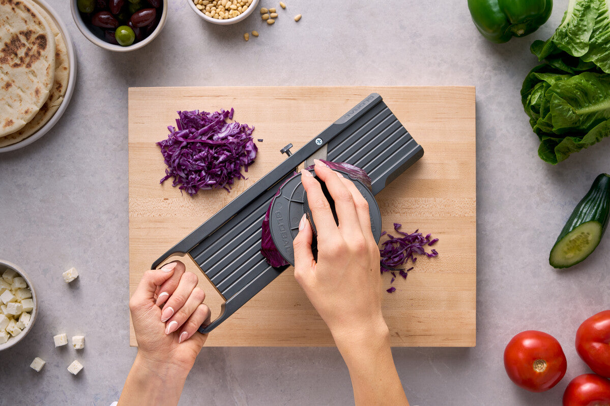 Chef using Global kitchen mandoline vegetable slicer for thinly slicing cabbage with protective finger guard for safe food prep.