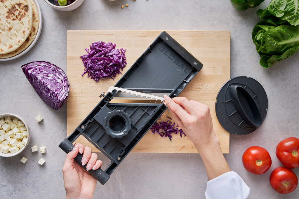 Back view of Global's stainless steel mandolin slicer showing cook easily changing interchangeable blade attachment for julienne cuts of vegetables.
